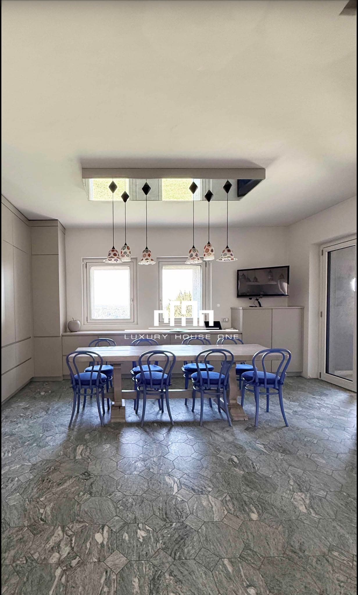Sala da pranzo moderna con tavolo in legno, sedie blu e pavimento in pietra esagonale.